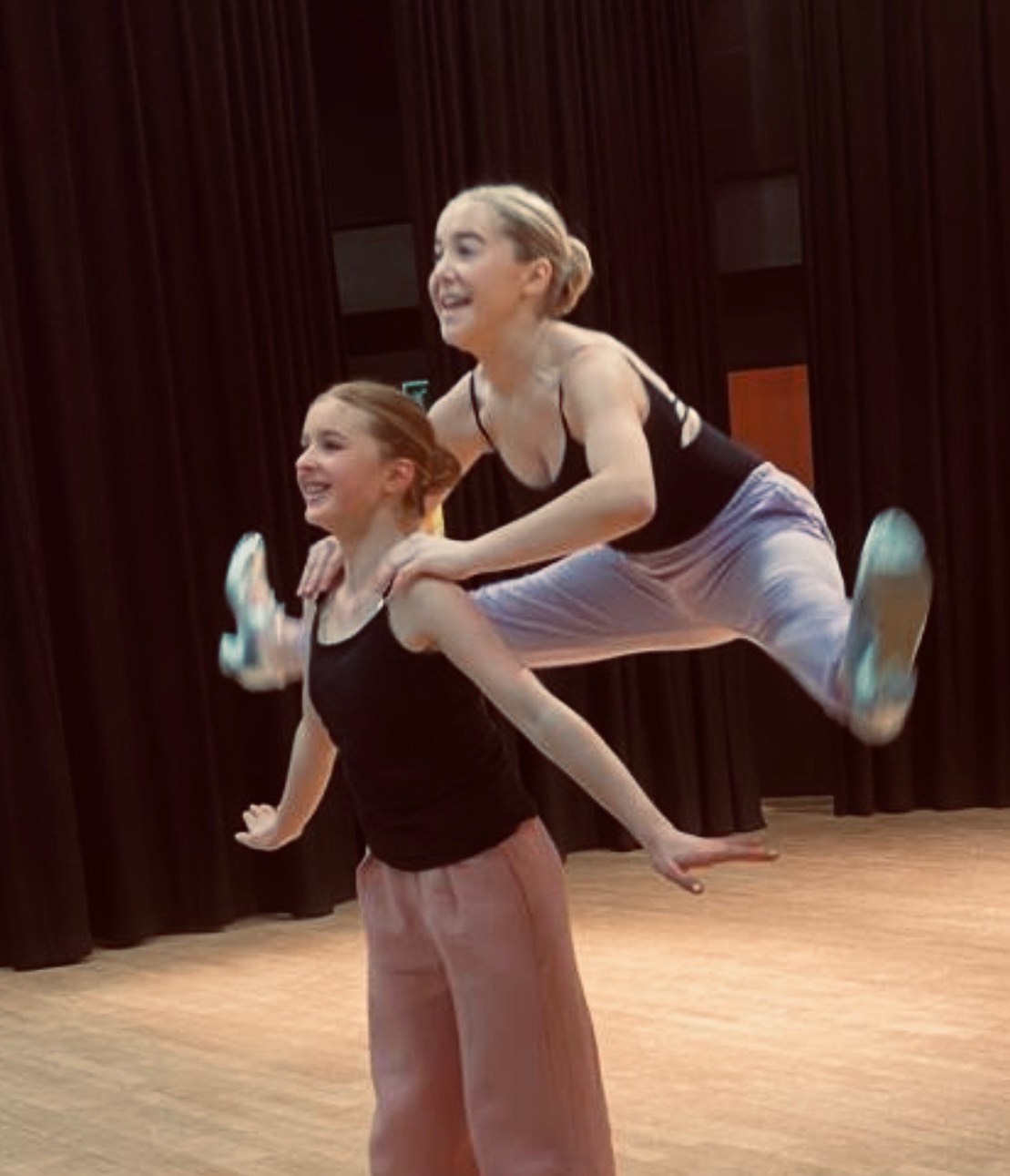 two girls performing a ballet move where one jumps behind the other with legs in splits