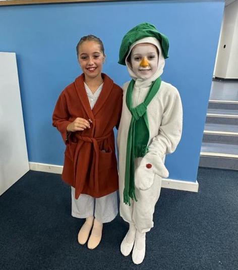 a girl in a dance uniform and dressing gown with her arm around a girl dressed as a snowman